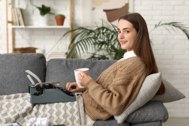 Evdeki kanepede yatıp daktilo ve çay içen mutlu kadın yazar.