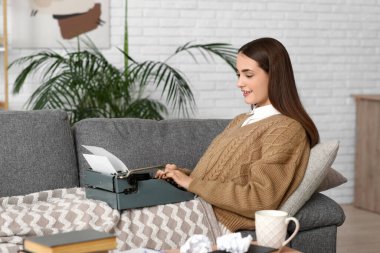 Evdeki kanepede daktilosu olan güzel, mutlu bir kadın yazar.