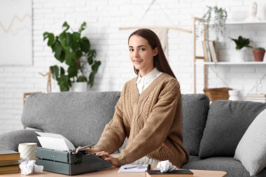 Evdeki kanepede oturan daktiloyla ve defteriyle güzel, mutlu bir kadın yazar.