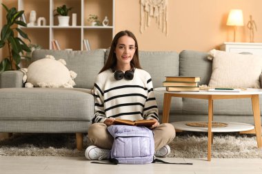 Kitaplar, sırt çantaları ve kulaklıkları evde okuyan güzel, mutlu bir bayan öğrenci.