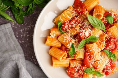 Bir tabak lezzetli makarna, domates ve fesleğenli, yakın plan.