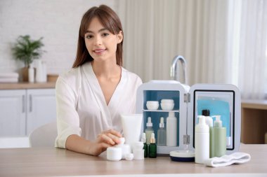 Tuvaletteki kozmetik ürünleri için küçük buzdolabı olan güzel genç bir kadın.