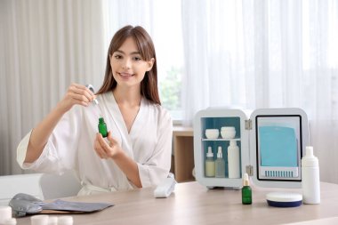 Küçük buzdolabı ve kozmetik ürünleriyle banyoda güzel bir genç kadın.