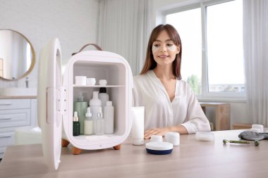 Küçük buzdolabı ve kozmetik ürünleriyle banyoda güzel bir genç kadın.