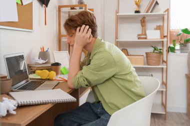 Stresli erkek öğrenci masada ders çalışıyor.