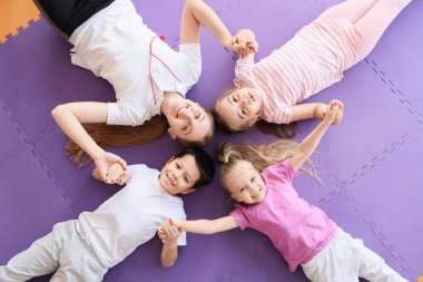 Spor salonundaki paspasın üstünde el ele tutuşan küçük sevimli çocuklar.