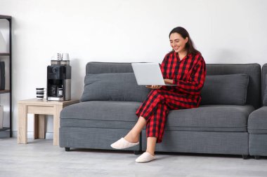 Ofisteki kanepede dizüstü bilgisayarla çalışan genç bir iş kadını. Ulusal İş Günü Pijamalarınızı Giyin