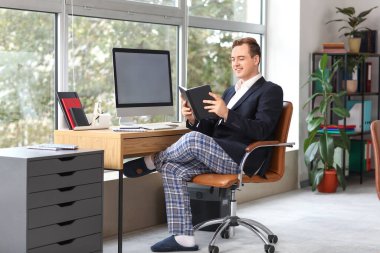 Masada çalışan defterli genç bir iş adamı. Ulusal İş Günü Pijamalarınızı Giyin