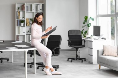 Ofiste çalışan dosyasıyla genç bir iş kadını. Ulusal İş Günü Pijamalarınızı Giyin