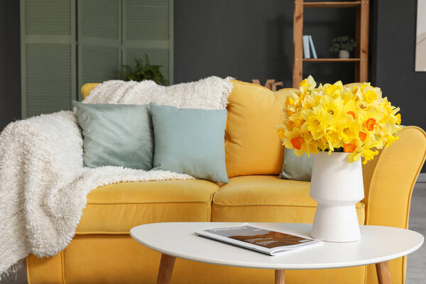Yellow sofa, plaid, vase with flowers and coffee table in living room