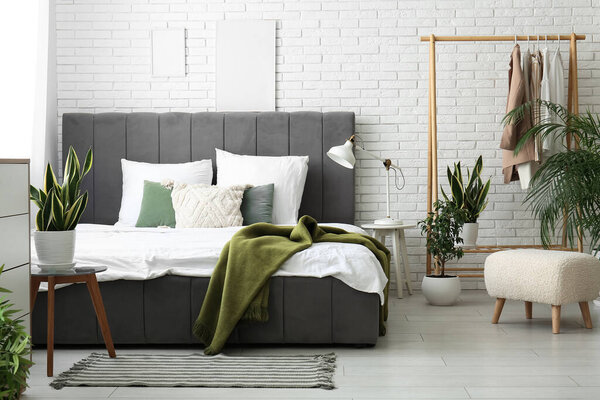 Stylish bed, houseplants and pillows in beautiful bedroom