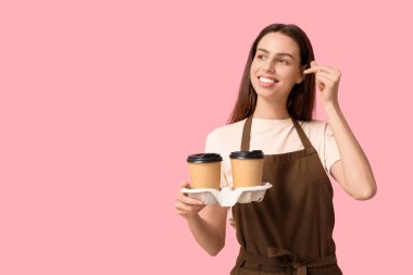 Kahveli genç bayan barista pembe arka planda kalp hareketi yapıyor.