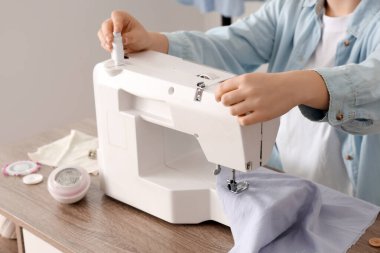 Atölyedeki masanın yanında dikiş makinesi kullanan genç bir terzi.