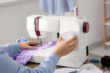 Genç bayan terzi atölyede, yakın plan masadaki leylak kumaş için dikiş makinesi kullanıyor.