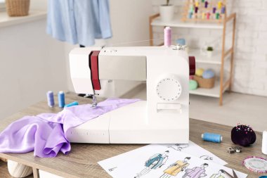 Atölyedeki terzi malzemeleri ve leylak kumaşlı modern dikiş makinesi.