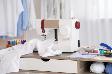 Beyaz gömlekli modern dikiş makinesi ve atölyedeki terzi malzemeleri.