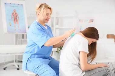 Olgun kadın osteopat klinikte genç bir bayanla masaj yapıyor.