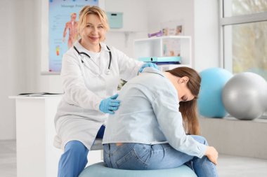 Olgun, mutlu kadın osteopat klinikte sağlıklı genç bir kadınla çalışıyor.