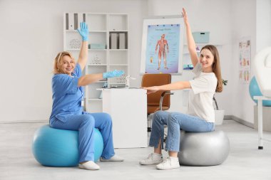 Olgun, mutlu bir kadın osteopat ve klinikte toplar üzerinde egzersiz yapan genç bir kadın.