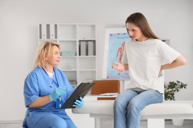 Kanepede genç bir kadın klinikte elinde panoyla olgun bir kadın osteopatına gidiyor.