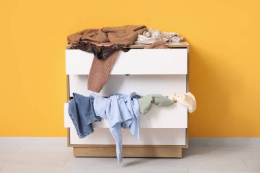 Sarı duvarın yanında farklı dağınık kıyafetlerle şık bir tuvalet.