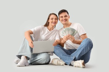 Parası ve dizüstü bilgisayarı olan genç çift arka planda oturuyor.