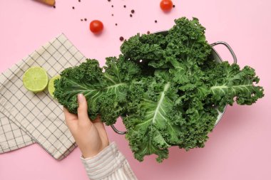 Taze lahana yapraklı süzgeç, limon ve domatesli pembe arka planda kadın eli.