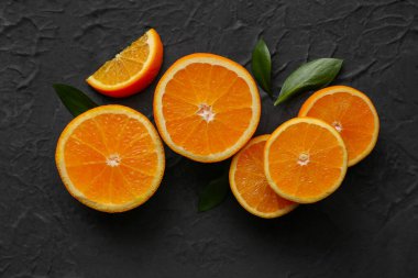 Taze olgun portakal dilimleri ve siyah arka planda yapraklar.
