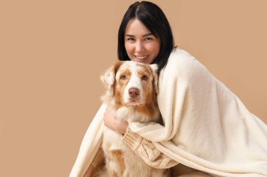 Tatlı Avustralya çoban köpeği ve bej arka planda battaniyesi olan genç bir kadın.