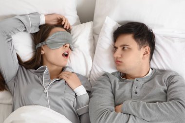 Evde horlayan karısıyla yatakta yatan sinirli genç bir adam.