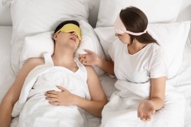 Horlayan kocasıyla yatakta yatan genç, rahatsız bir kadın.