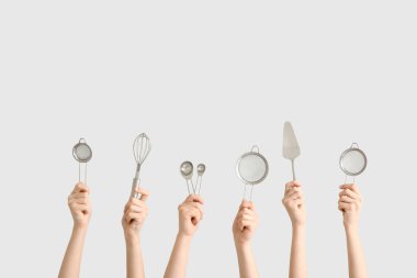 Beyaz arka planda kaşık, çırpma ve pasta spatulası ile süzgeçleri tutan kadın eller.