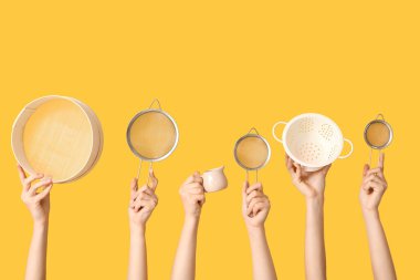 Sarı arka planda süt testisi ve süzgeçli süzgeçleri tutan kadın eller.