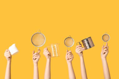 Female hands holding sieves with milk jug and measuring cup on yellow background clipart