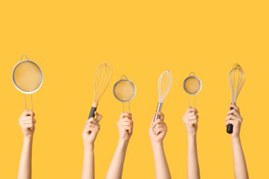 Sarı arka planda süzgeçleri ve çırpıcıları olan kadın elleri