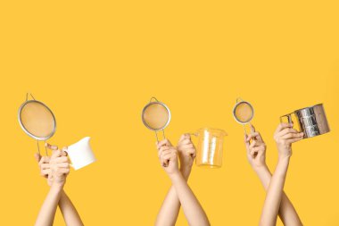 Female hands holding sieves with milk jug and measuring cup on yellow background clipart