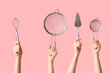 Pembe arka planda fırça ve pasta spatulasıyla süzgeçleri tutan kadın eller.