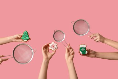 Female hands holding sieves with Christmas cookies on pink background clipart