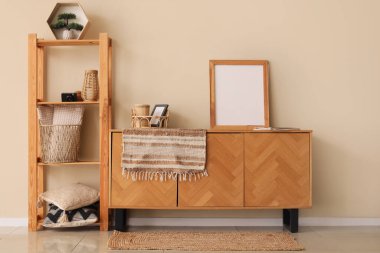 Modern odanın içinde şık bir şifoniyer ve bej duvarın yanında raflar var.