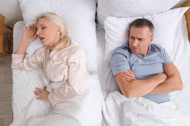 Memnun olmayan olgun bir adam horlayan karısıyla yatakta uzanıyor.