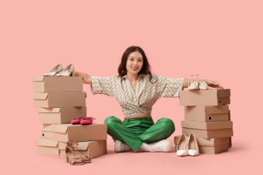 Pembe arka planda oturan ayakkabı kutularıyla genç Asyalı kadın.