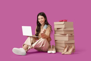 Dizüstü bilgisayarı ve kredi kartı olan genç bir kadın mor arka planda ayakkabı alıyor.