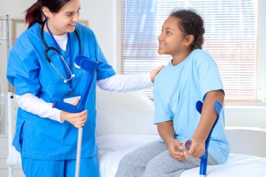 Hastane odasında koltuk değnekleri olan Afro-Amerikalı bir kız ve doktor.