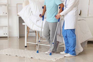 Koltuk değnekli genç bir kız ve hastane odasında yürüyen bir doktor.