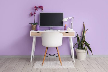 Ofiste içi boş bilgisayar monitörü ve leylak duvarının yanında orkide çiçeği olan bir işyeri