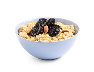 Beyaz zemin üzerinde kuru erik ve badem olan bir kase lezzetli yulaf ezmesi.