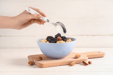 Beyaz ahşap arka planda kuru erik ve bademle lezzetli yulaf ezmesi yiyen bir kadın.