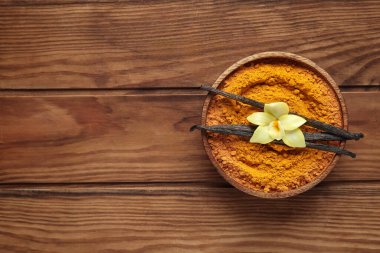 Bir kase zerdeçal tozu, vanilya çubukları ve ahşap arka planda çiçek.