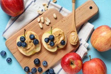 Lezzetli elma dilimli ahşap tahta, fındık ezmesi, yabanmersini ve mavi arka planda fıstık.