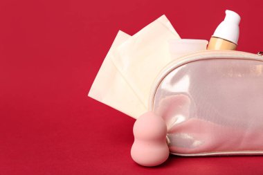 Kırmızı arka planda regl fincanı, ped ve makyaj ürünleri bulunan kadının makyaj çantası.